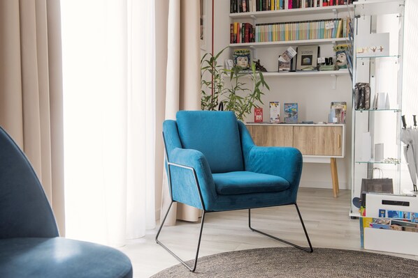 Una sala de estar moderna con un sillón azul, una estantería y una mesita de madera.