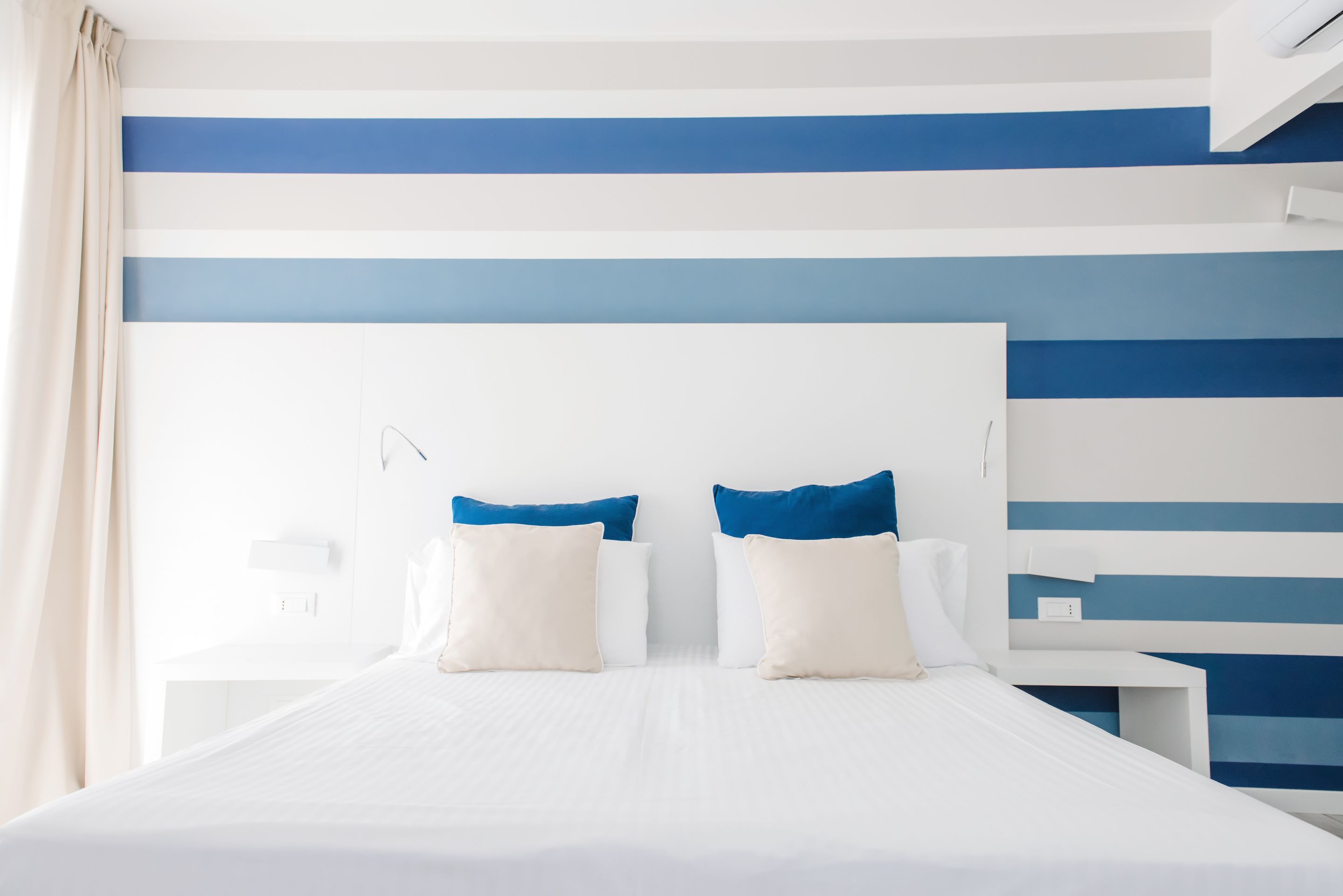 A hotel room with a large bed, two bedside tables, and a headboard with a blue and white striped pattern.
