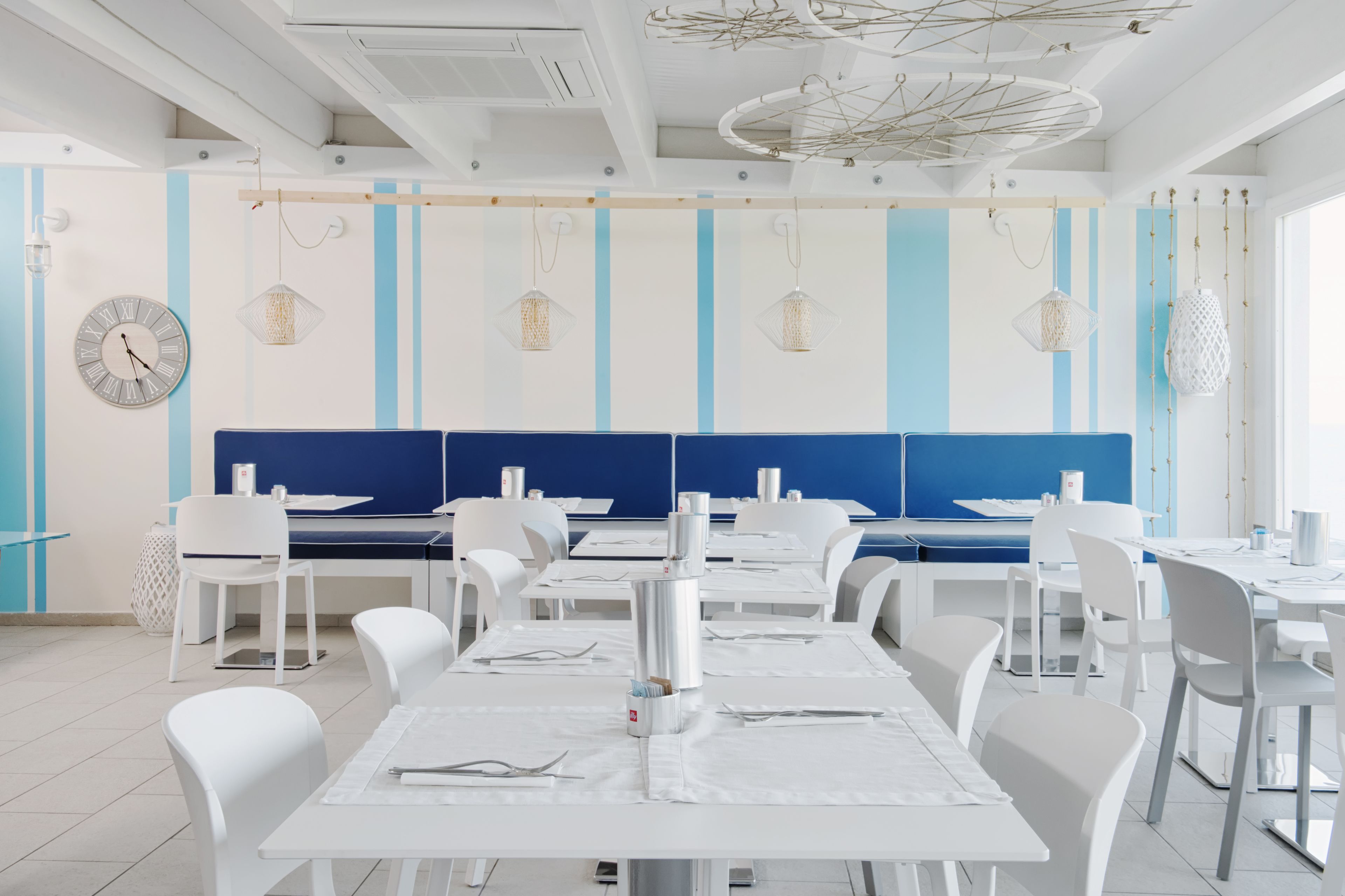 A modern dining area with white tables and chairs, a blue accent wall, and hanging pendant lights.