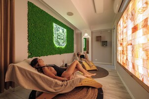 Un cuarto de spa con dos camillas de masaje, una pared verde con un logotipo y una pared grande con un diseño texturizado.