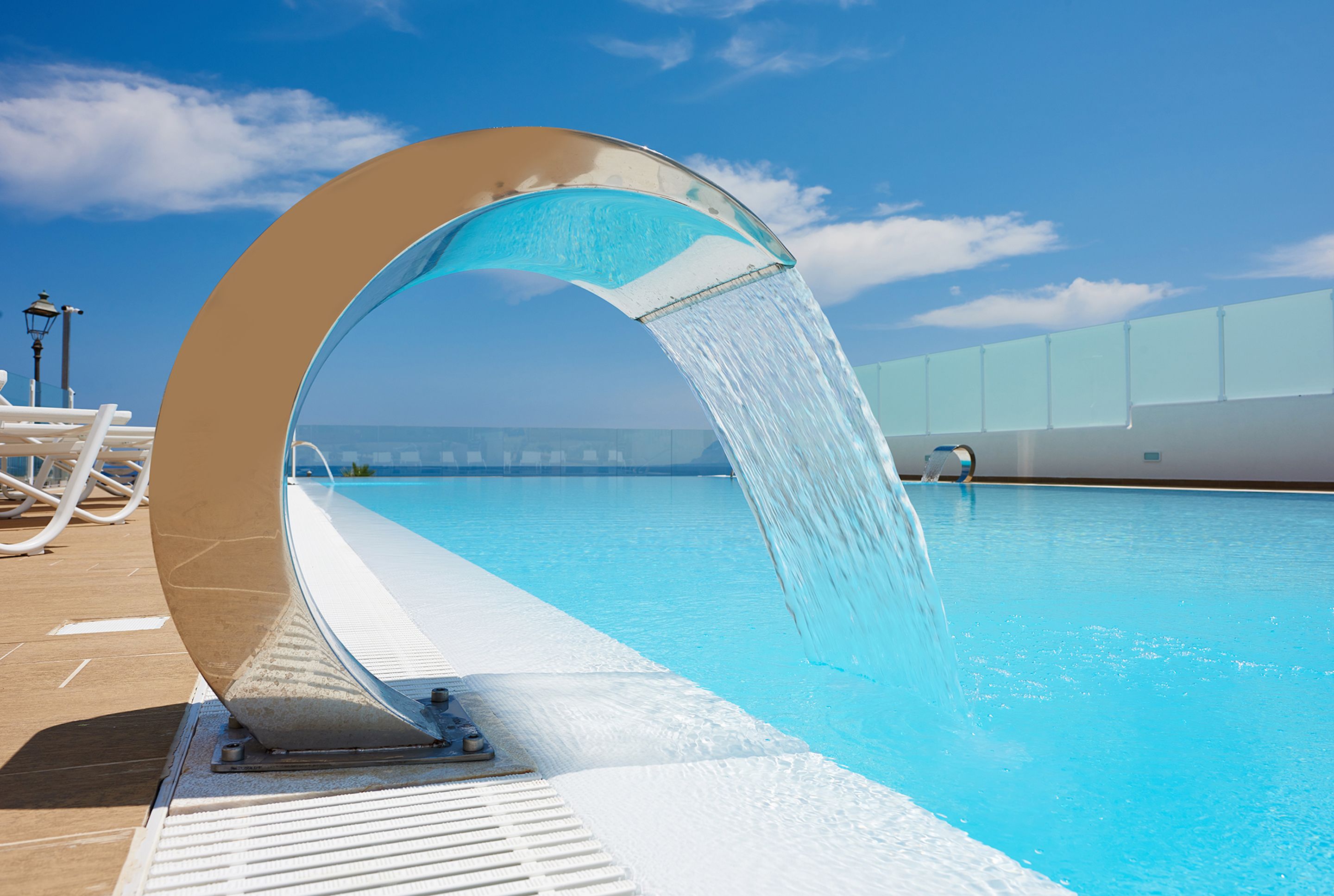 A pool with a water feature and a clear view of the ocean.