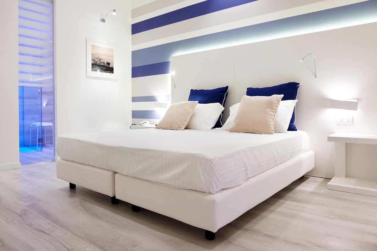 A modern bedroom with a large bed, a bedside table, and a wall-mounted light fixture.