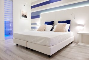 A modern bedroom with a large bed, a bedside table, and a wall-mounted light fixture. - Marina di Petrolo Hotel & SPA (Castellammare del Golfo)