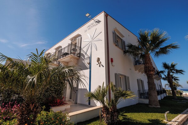 A white building with a palm tree and flowers in the foreground, a balcony, and a sign reading "Marina di Petrolio". - Marina di Petrolo Hotel & SPA (Castellammare del Golfo)