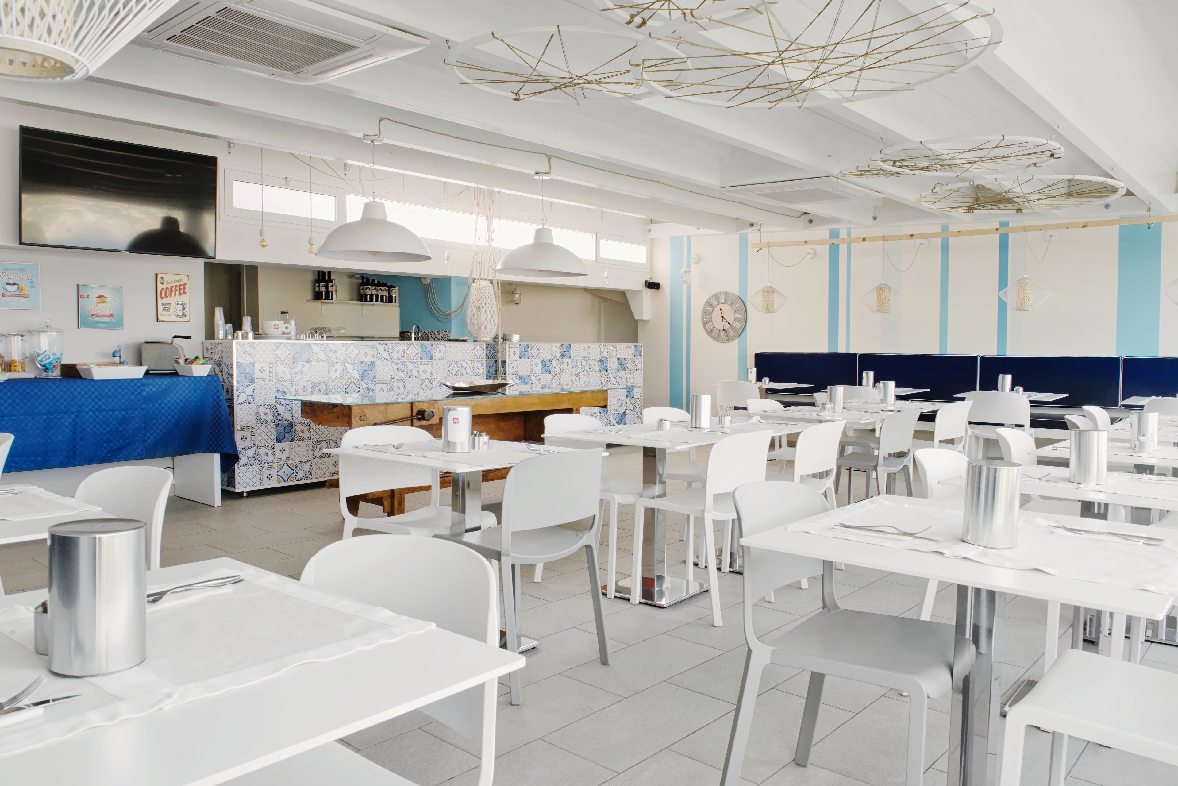 Un ristorante con tavoli e sedie bianche, una parete rivestita di piastrelle blu e bianche e un orologio a parete.