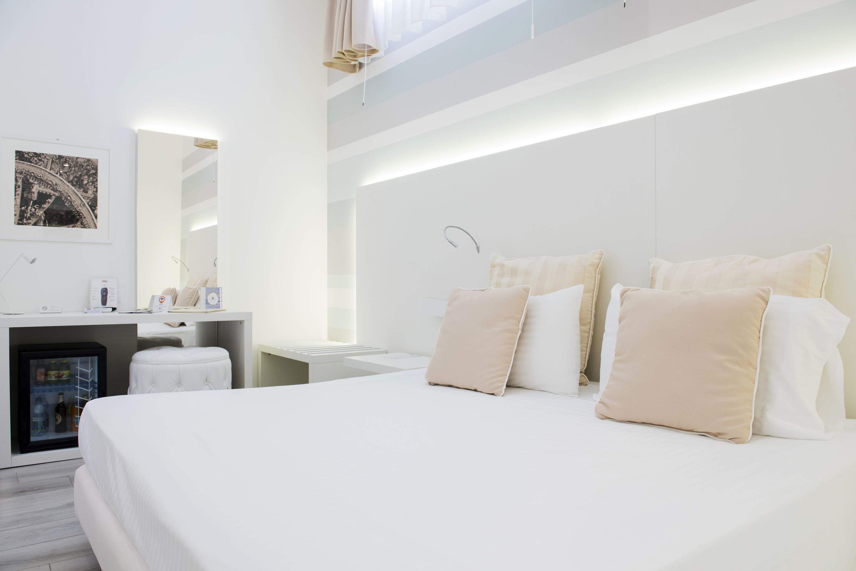 A modern hotel room with a large bed, a small desk, a minibar, and a large window.