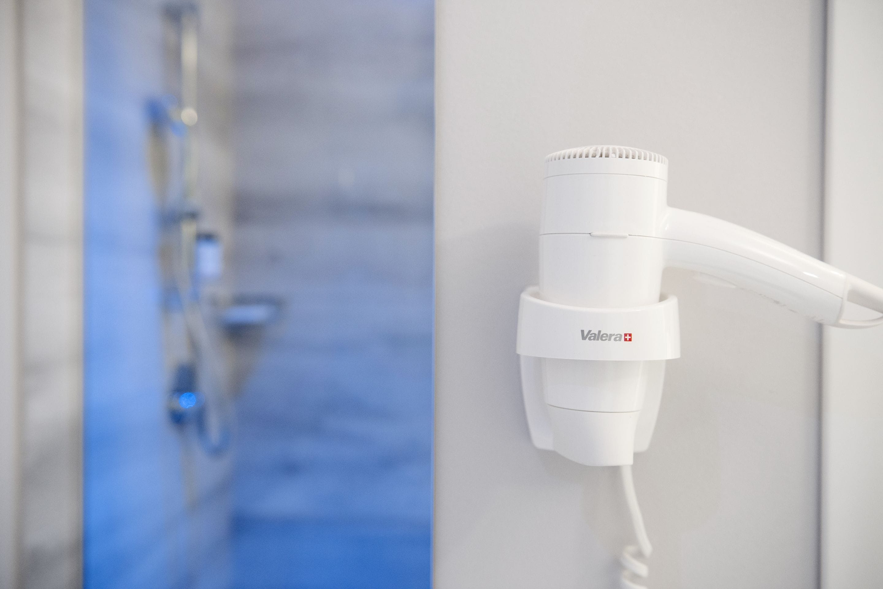 Un secador de pelo blanco montado en la pared, con un panel de control a la vista y un cable.