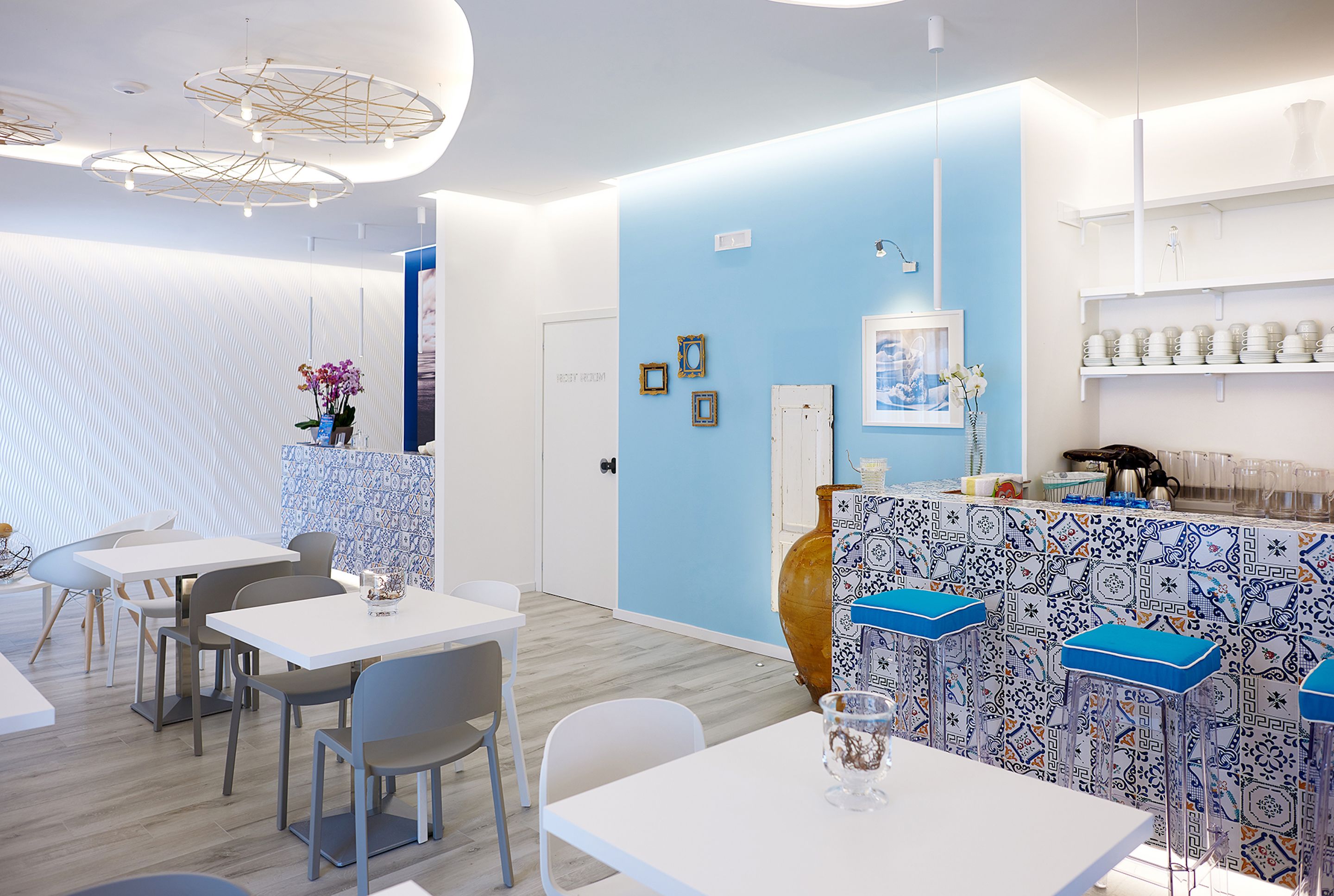 A modern restaurant interior with white tables, blue walls, and patterned bar stools.