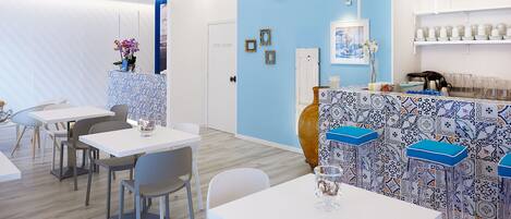 A modern restaurant interior with white tables, blue walls, and patterned bar stools.