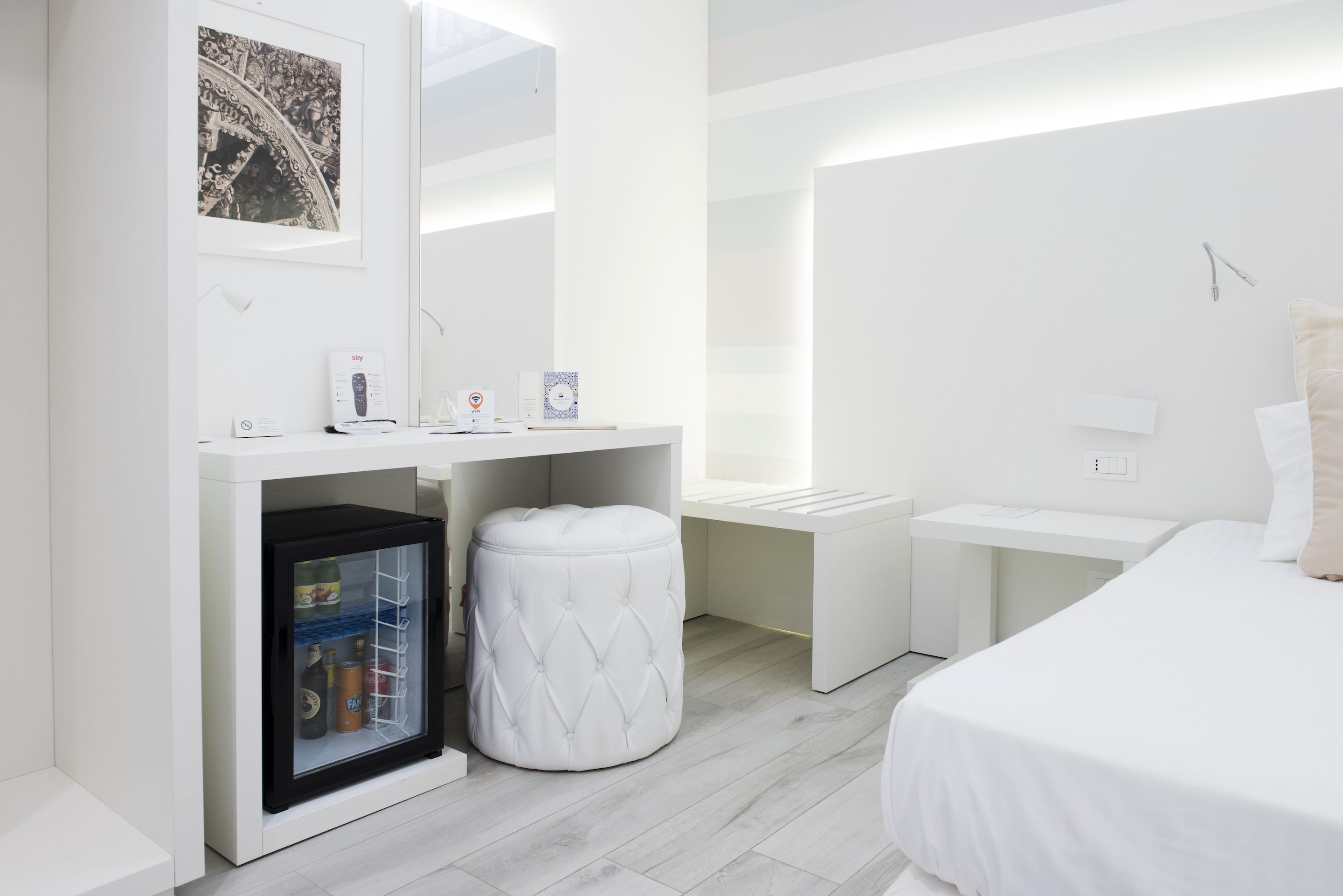 Habitació d'hotel moderna amb nevera, petit otomà, taulella de nit i llit.