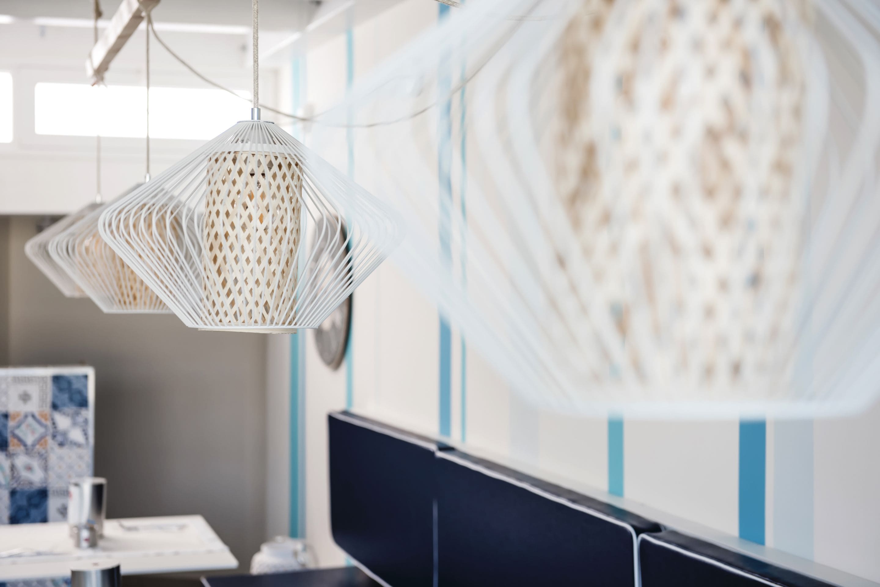 A modern office space with a hanging white woven light fixture, a black desk, and a blue-striped wall.