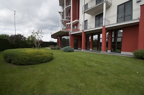 A modern building with a red and white facade, multiple balconies, and a well-maintained lawn with hedges. - Brindor Hotel (Poirino)