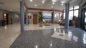 A spacious lobby with a tiled floor, large pillars, a reception desk, seating area, and a mural on the wall. - Brindor Hotel (Poirino)