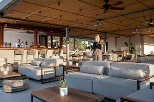 An outdoor seating area with sofas, chairs, and tables. There are ceiling fans and a bar area in the background.