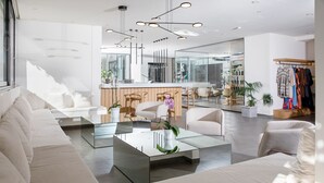 A modern living room with a glass coffee table, white sofas, and a wooden reception desk. - Almyrida Resort (Apokoronas)