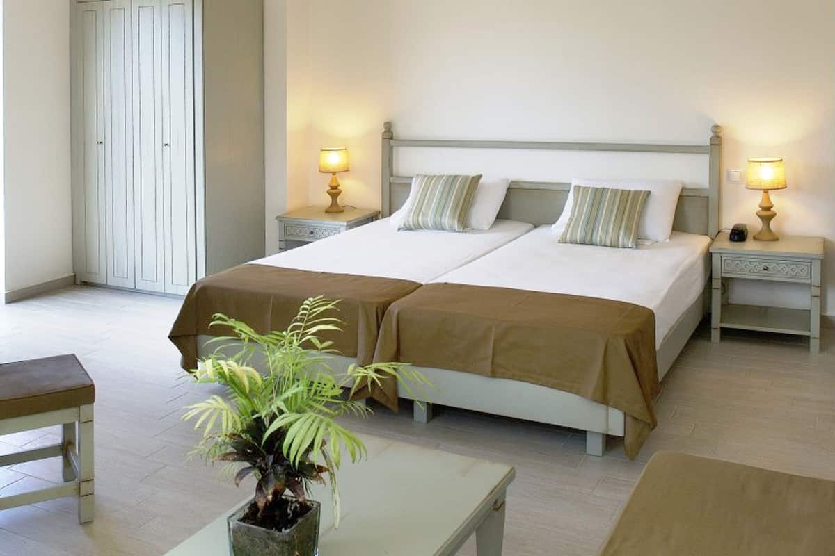 Una habitación doble con dos camas, mesitas de noche con lámparas, una planta en maceta y un banco de madera.