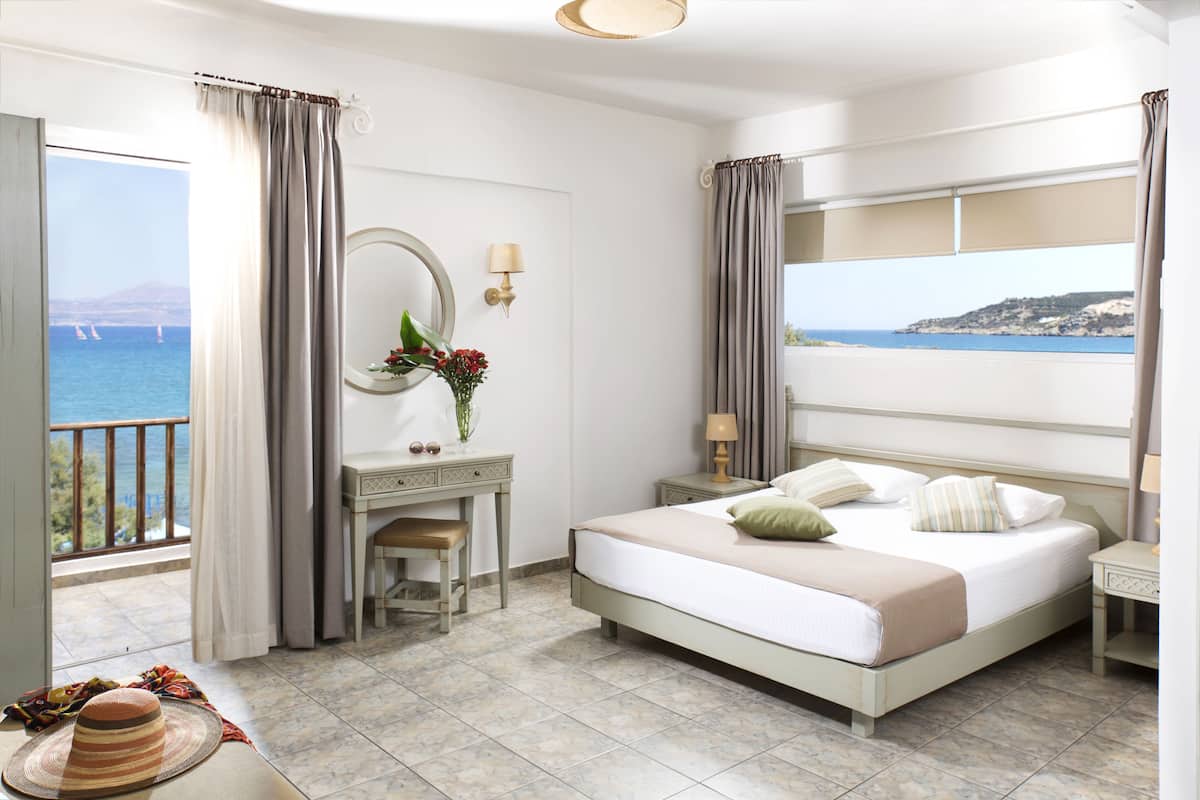 Habitación de hotel con cama, escritorio, silla, tocador con espejo y vista al mar.