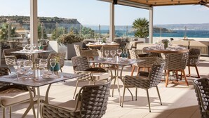 An outdoor dining area with tables and chairs, overlooking a scenic view of the sea and hills. - Almyrida Resort (Apokoronas)