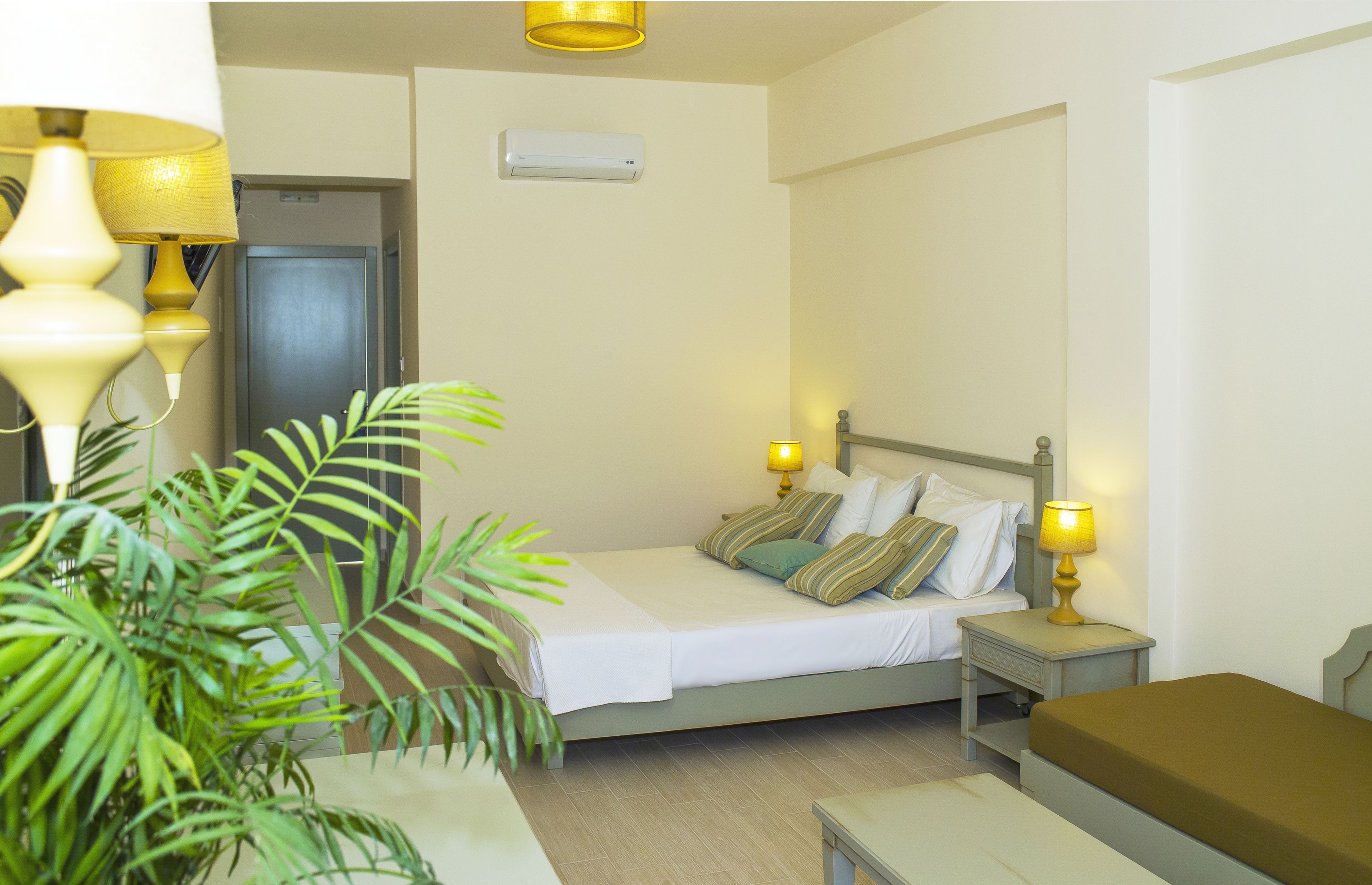 A hotel room with a bed, bedside tables, a lamp, and a potted plant.