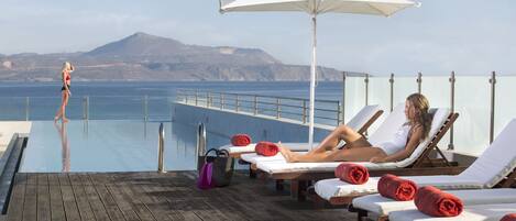 Zona junto a la piscina con sillones de descanso, una terraza de madera y vistas al mar y a las montañas.