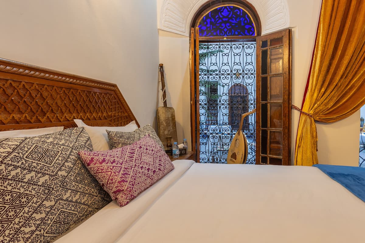 A bed with patterned pillows, a wooden headboard, and a view of a blue-lit door with a decorative window.