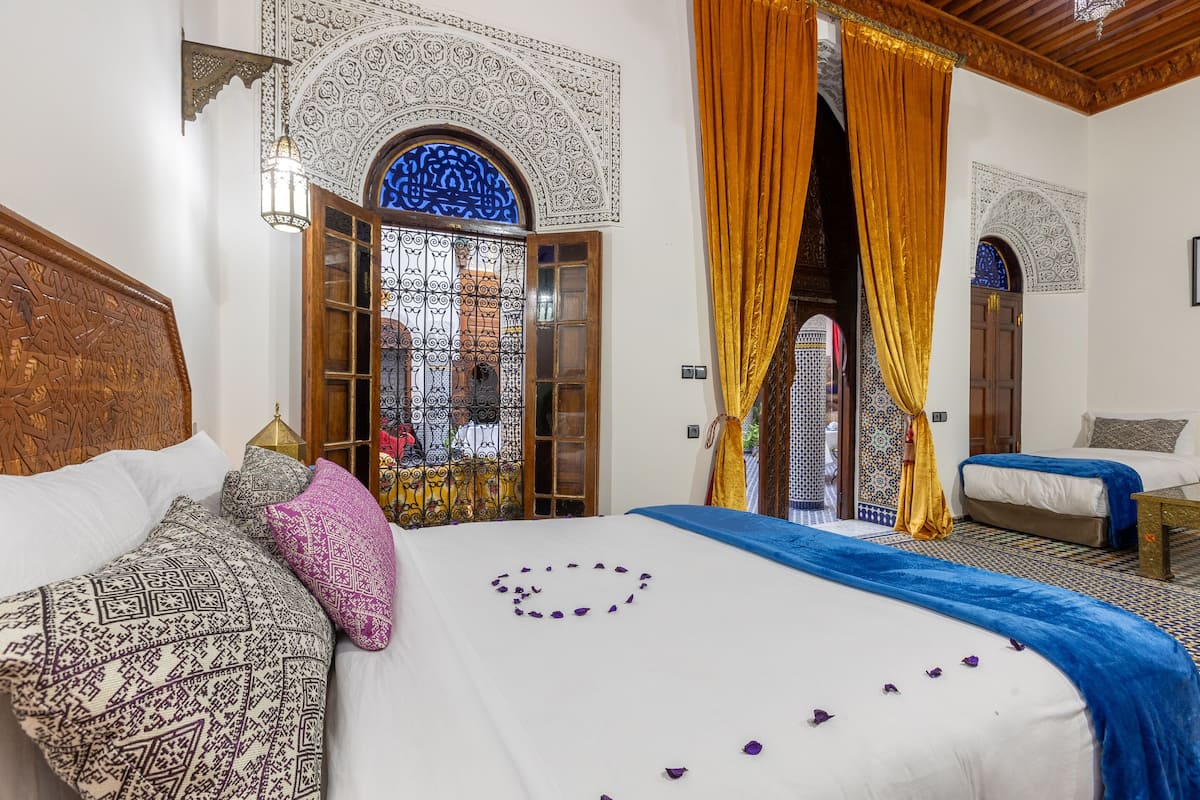 A room with a bed, a sofa, and a window with intricate patterns.