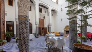 A traditional Moroccan interior with patterned tile floors, ornate columns, and a dining area with tables and chairs. - Palais Nazha Fes - Luxury Lodging (Fes)