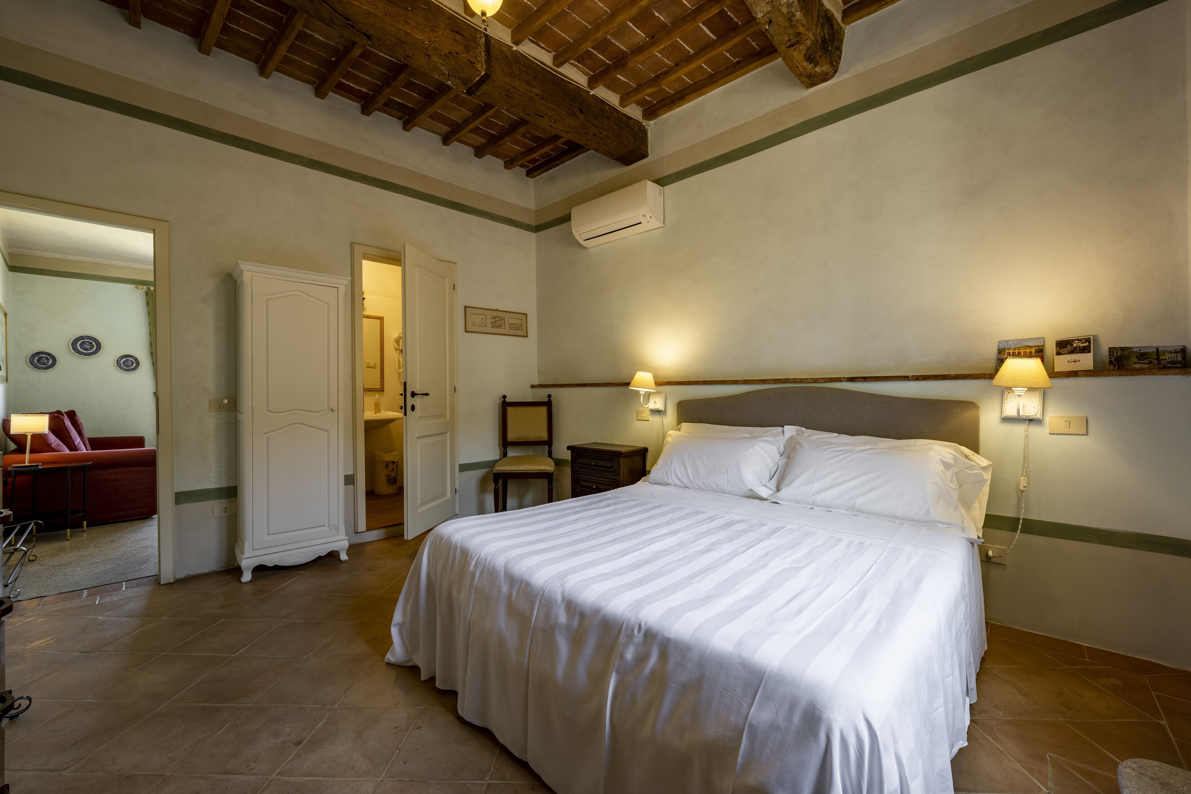 A bedroom with a large bed, a wooden ceiling, a white wardrobe, and a nightstand with a lamp.