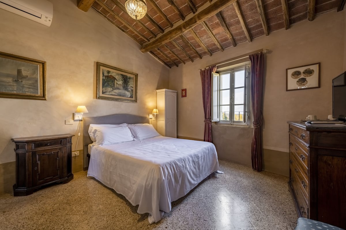 Une chambre à coucher avec un lit, une commode en bois et une fenêtre avec des rideaux.