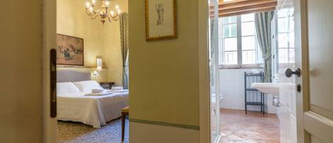 Ein Hotelzimmer mit Bett, einer Chandelier, einem gerahmten Kunstwerk und einem Badezimmer mit Waschbecken und Fenster.