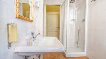 A bathroom with a white sink, a mirror, a shower enclosure, and a door leading to another room.