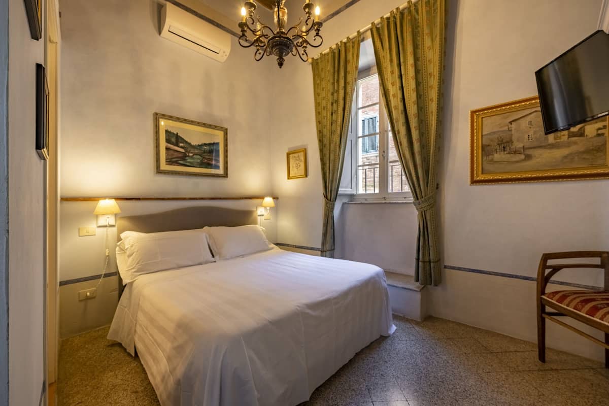Une chambre d’hôtel avec un lit, une chaise, une télévision et deux tableaux accrochés au mur.