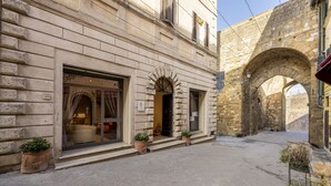 A stone building with a large arched doorway, potted plants, and a tiled courtyard. - Palazzo Mosela Alla Porta (Montepulciano)