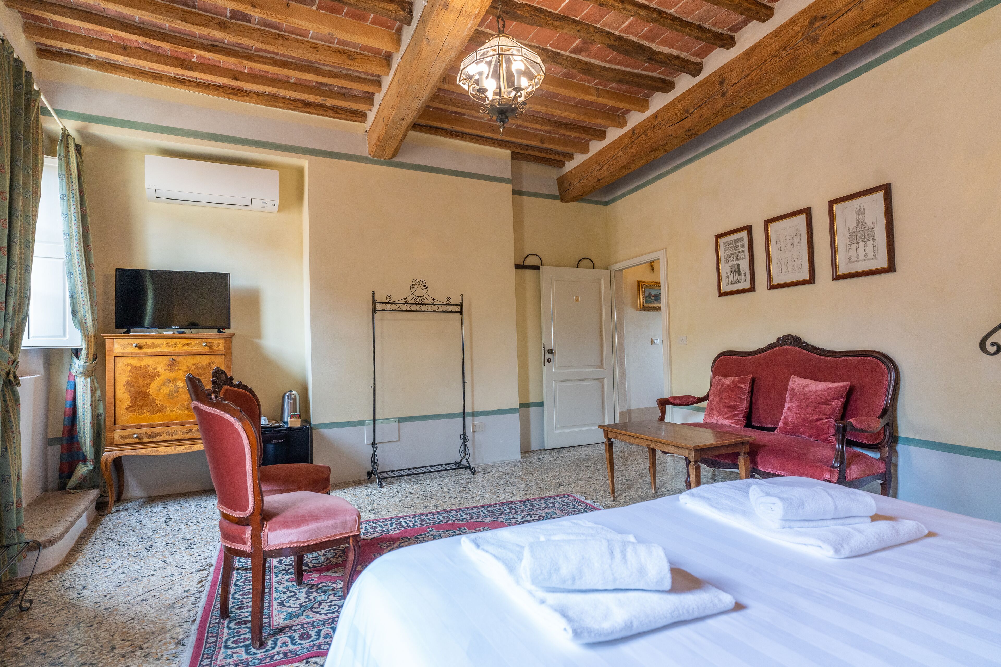 Une chambre d’hôtel comprenant un lit, un bureau, une chaise, une télévision, une armoire et un plafond avec des poutres apparentes.