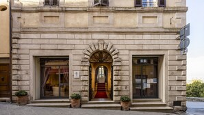 A historic building with a grand entrance, a red carpet, and two potted plants at the entrance. - Palazzo Mosela Alla Porta (Montepulciano)