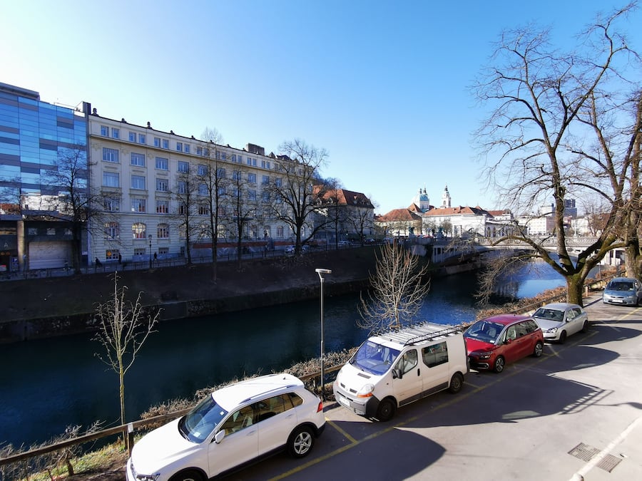Ein Parkplatz mit mehreren Autos, einem Fluss und Gebäuden im Hintergrund.