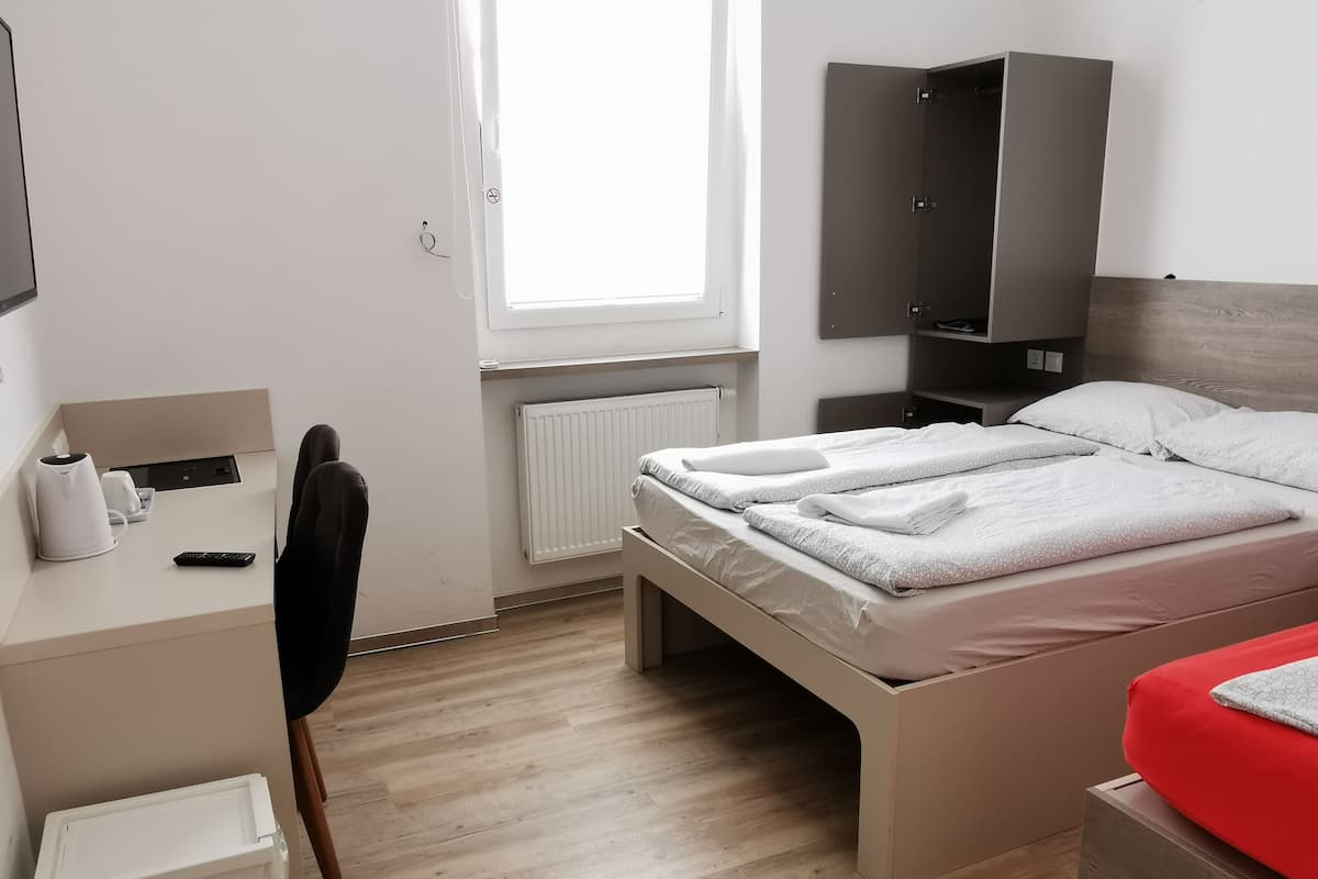 A modern hotel room with a bed, a desk, a chair, a wardrobe, and a window.