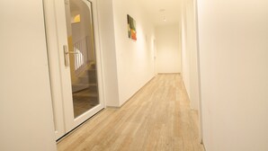 A hallway with a wooden floor, white walls, and a glass door leading to a staircase.