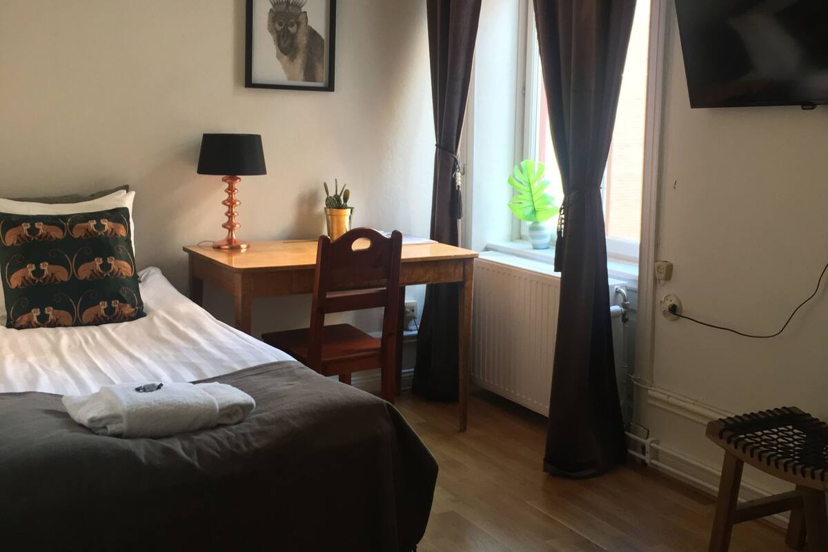 Hotellihuone, jossa on sänky, työpöytä, tuoli, televisio ja ikkuna, jossa on verhot.
