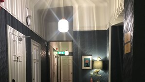 A hallway with wooden flooring, white doors, and a dark wall with a framed picture and a small table with a lamp. - Morris Hotel (Örebro)