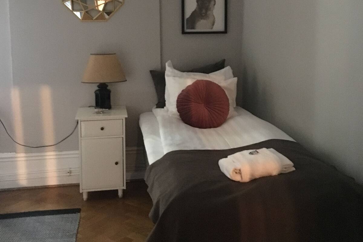 Makuuhuoneessa on sänky, yöpöytä, lamppu, peili ja seinällä oleva kehystetty kuva.