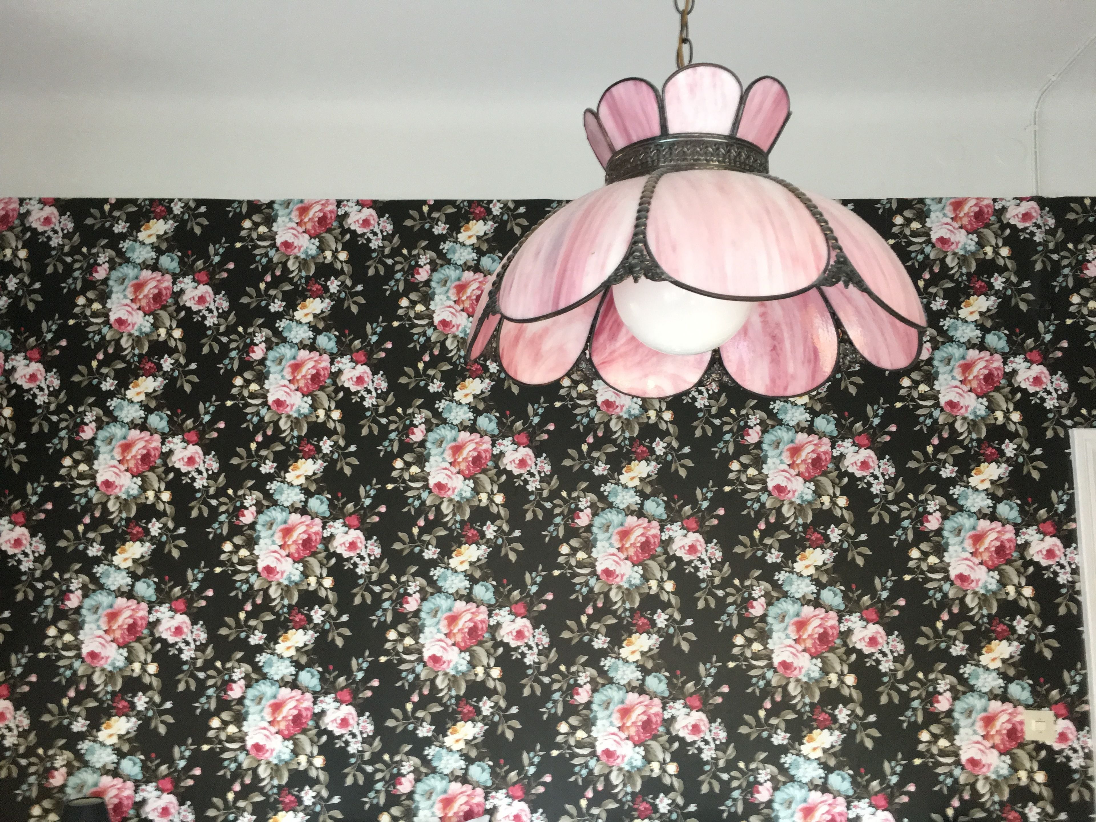 Una habitación con papel tapiz estampado con motivos florales y una lámpara de techo rosa con bordes ondulados.