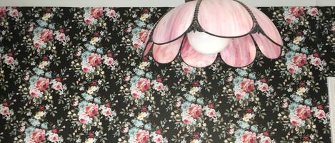 Una habitación con papel tapiz estampado con motivos florales y una lámpara de techo rosa con bordes ondulados.