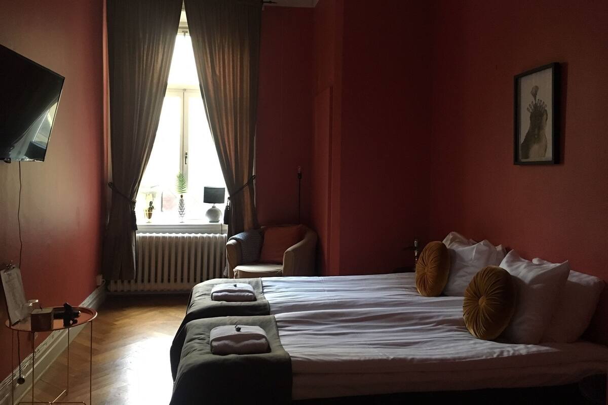 Hotellihuone, jossa on sänky, tuoli, pöytä ja ikkuna, jossa on verhot.