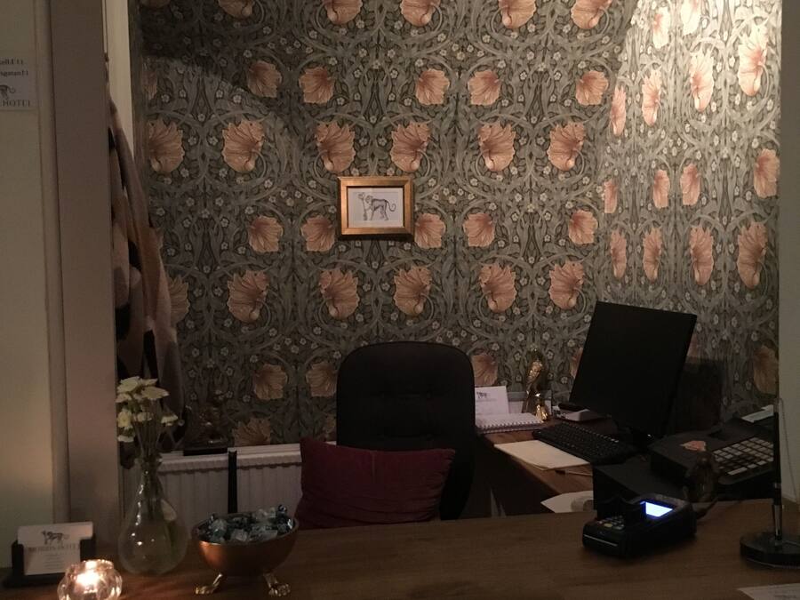 Et værelse med blomstret tapet, et skrivebord med en computer, en stol og et lille bord med en vase og en skål.