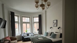 A bedroom with a bed, a sofa, a TV, and a window with curtains. - Morris Hotel (Örebro)