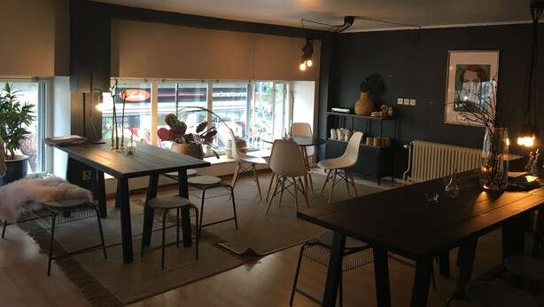 A modern dining area with a wooden table and chairs, a large window with a view of a restaurant, and a dark wall with a framed picture. - Morris Hotel (Örebro)