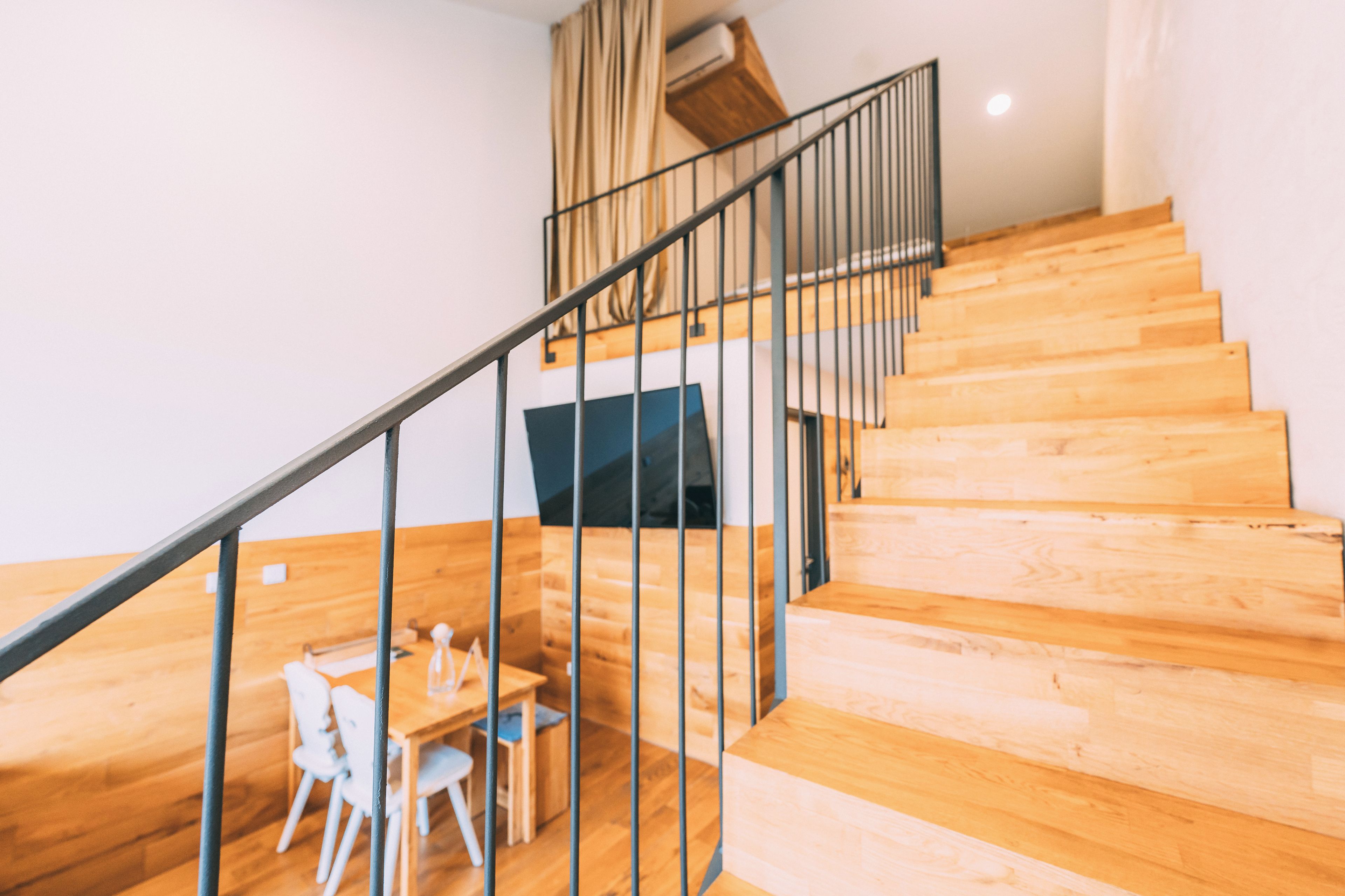 Un escalier avec des marches en bois et une rampe en métal, menant à une pièce où se trouvent un bureau et des chaises.