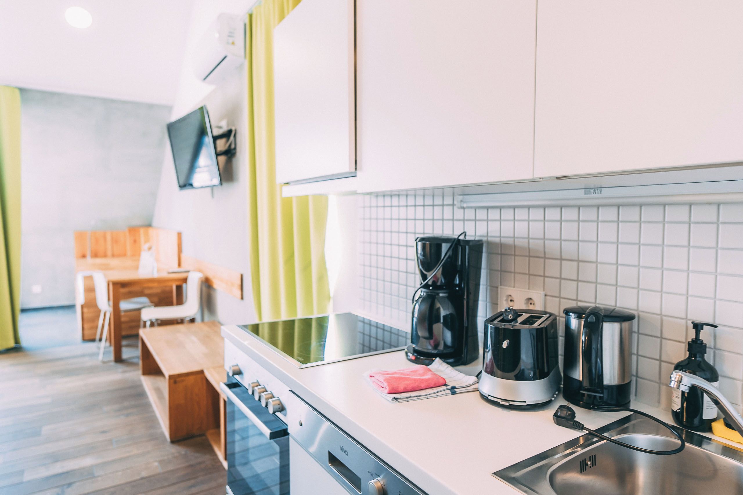 A modern kitchen with a sink, coffee maker, toaster, and a wooden table with chairs.