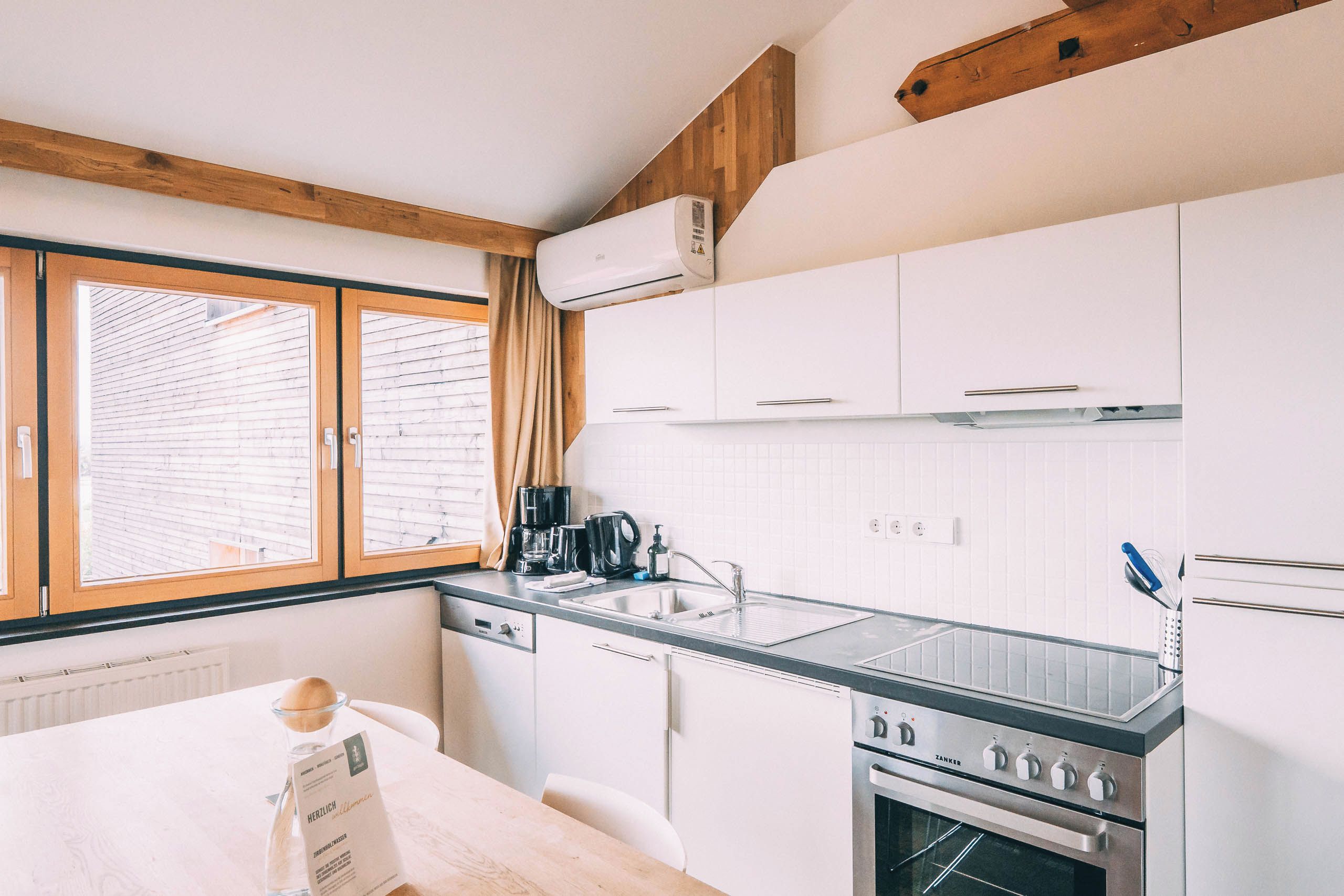 A modern kitchen with white cabinets, a stainless steel stove, and a window with blinds.